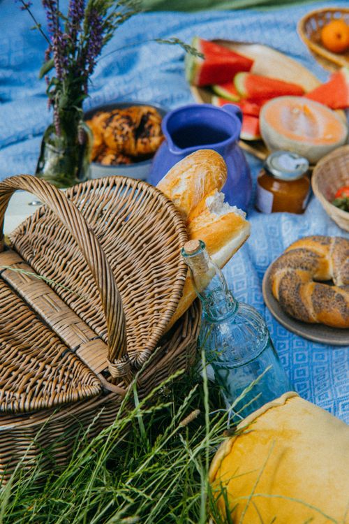 Free A vibrant outdoor picnic featuring breads, fruits, and a wicker basket on a blue blanket. Stock Photo