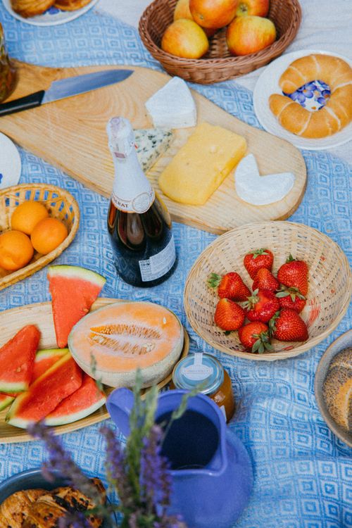 Free High-angle shot of a vibrant picnic setup featuring fruits, cheese, and champagne on a blue blanket. Stock Photo