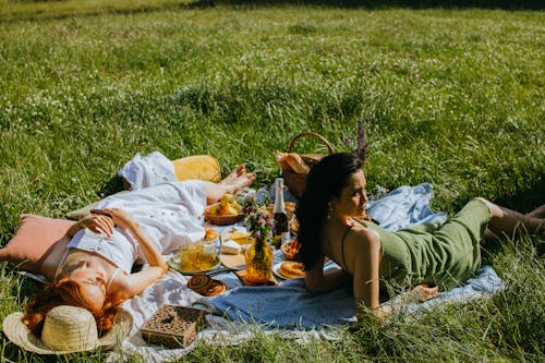 A Pair of Women Lying on Picnic Blanket with Food 