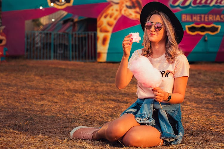 A Woman Sitting On Grass Eating Cotton Candy