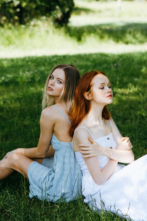 Free Two women sitting peacefully back to back on grass in summer attire Stock Photo
