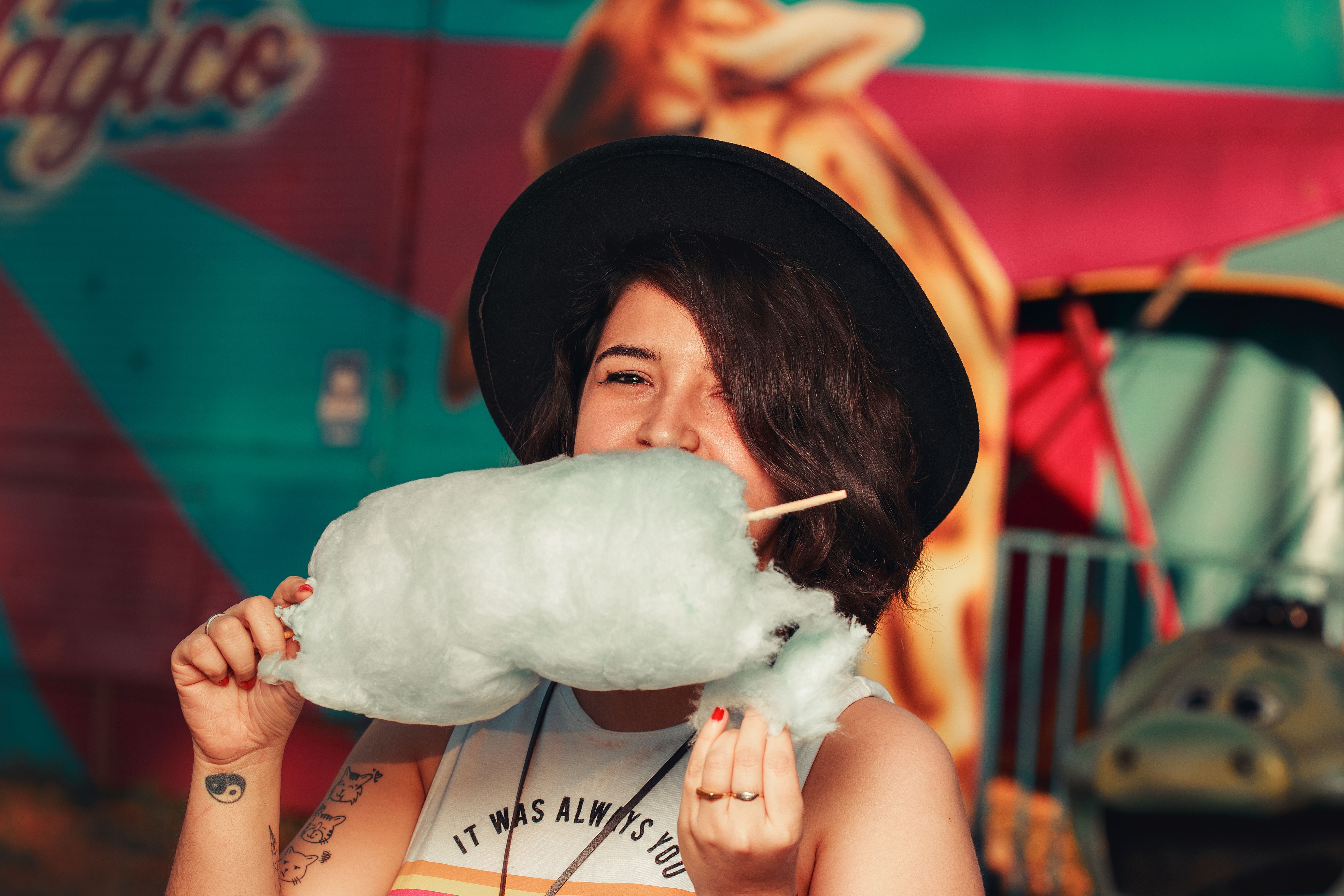 Young woman savoring cotton candy at a lively outdoor carnival scene.