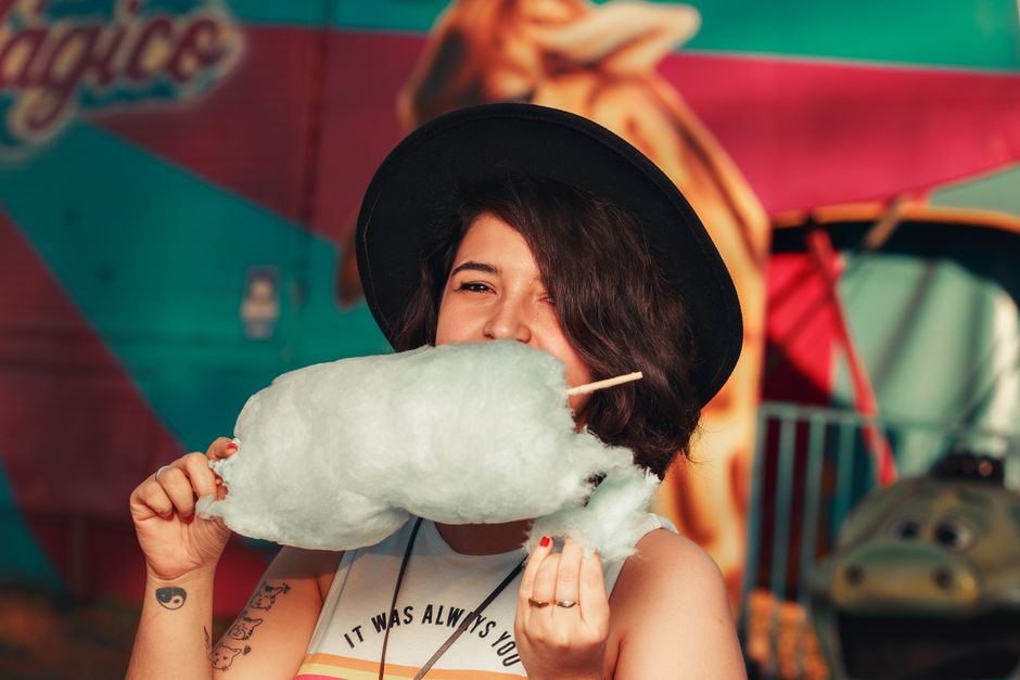 Young woman savoring cotton candy at a lively outdoor carnival scene.