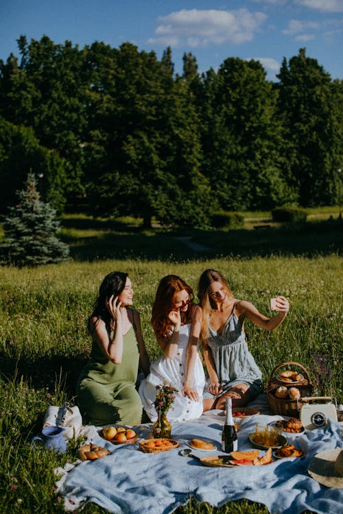 Free Three Women Sitting on the Grass while Taking Photo of Themselves Using a Cellphone Stock Photo