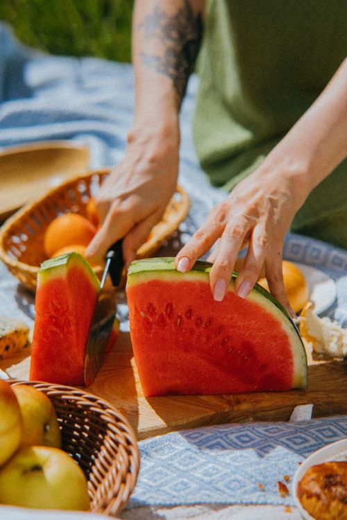 Free Hands slicing a fresh watermelon during a summer picnic with fruits on a blanket. Stock Photo
