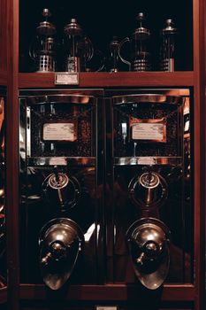 Elegant vintage coffee dispensers with French presses on wooden shelves in dim lighting.