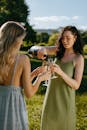 两名身穿绿色和蓝色连衣裙的女子在户外喝香槟庆祝