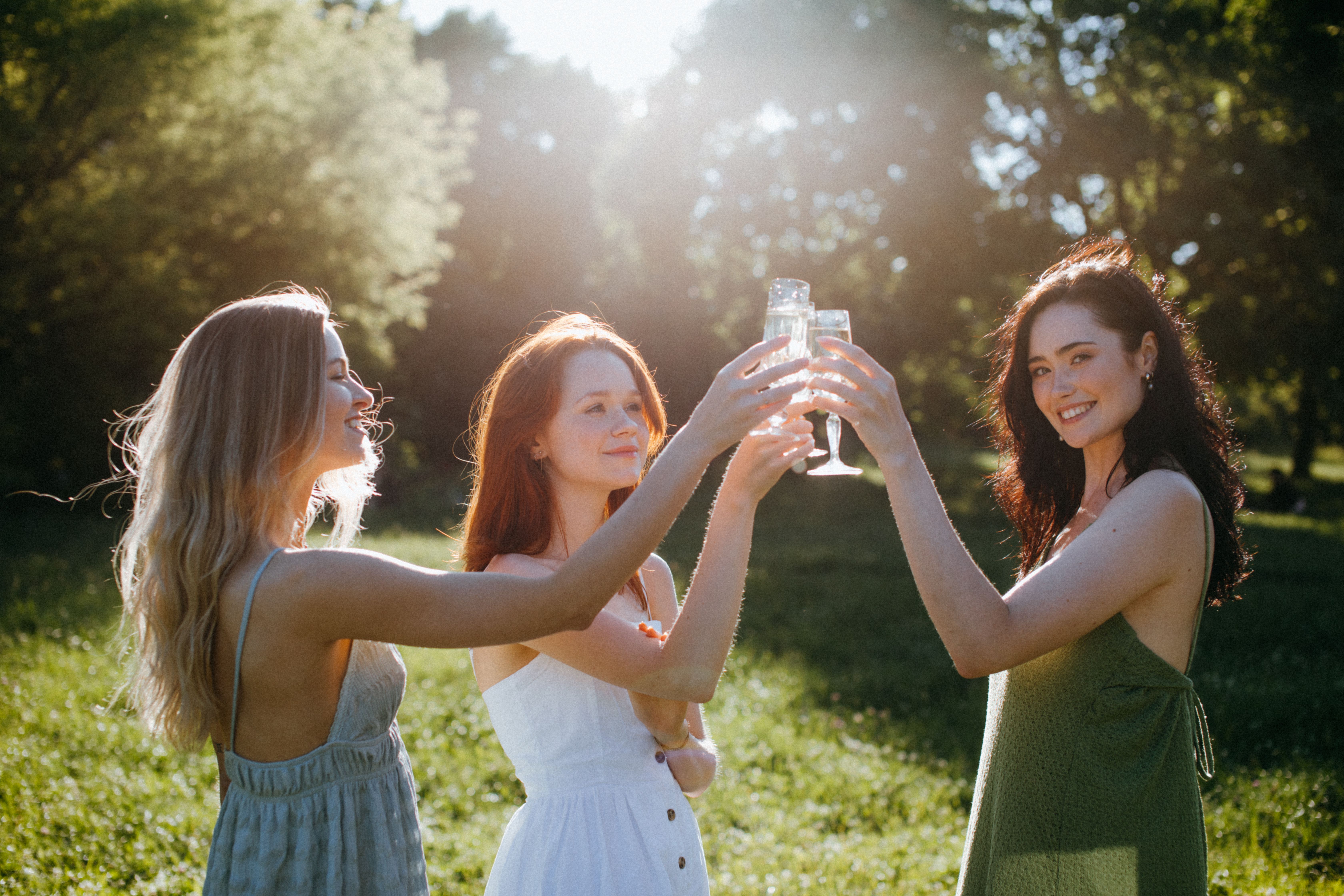 Trois amies trinquent au champagne en robes bohème lors d'un enterrement de vie de jeune fille en plein air