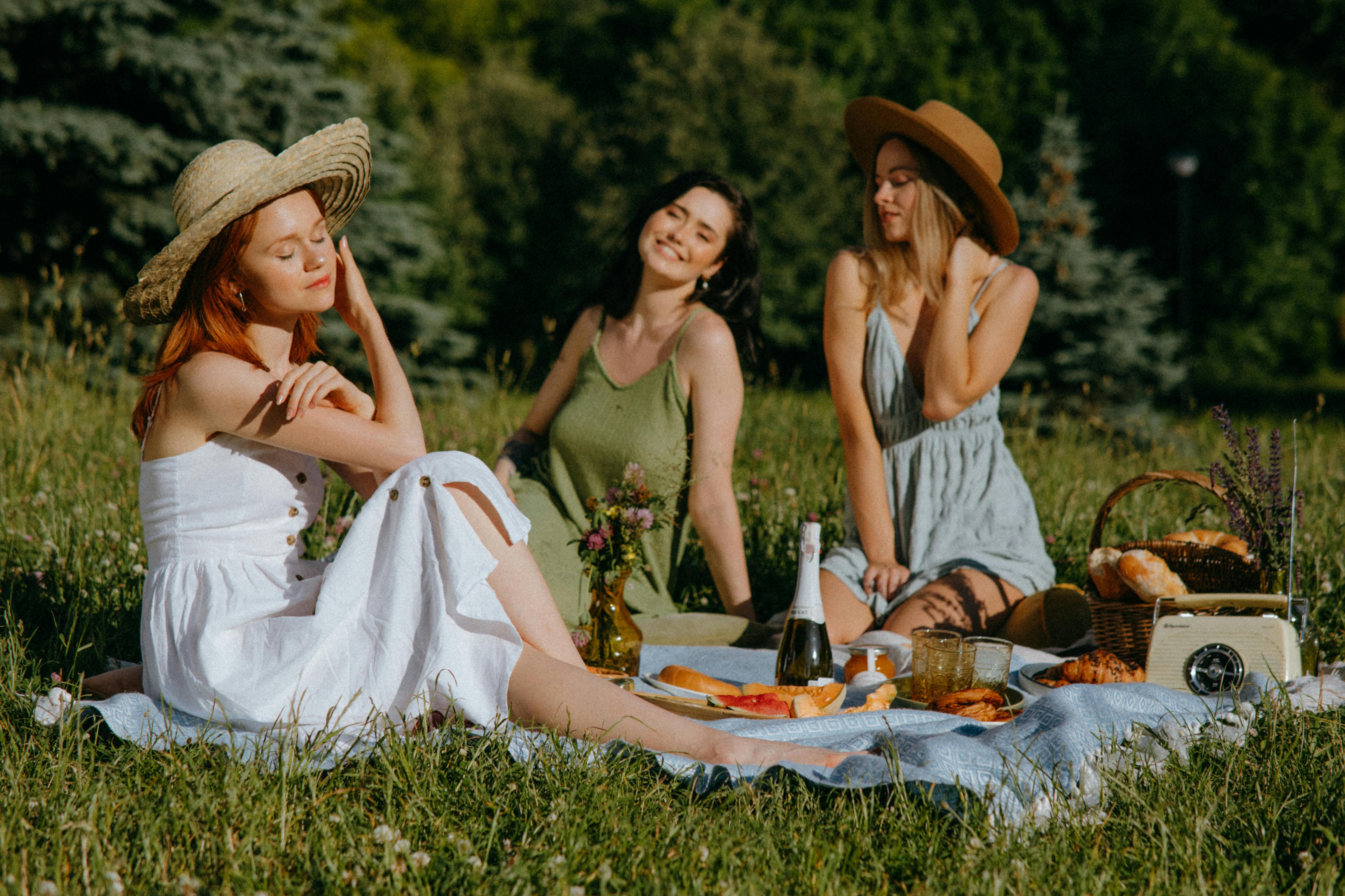Three friends enjoying a sunny picnic outdoors with food, laughter, and nature.