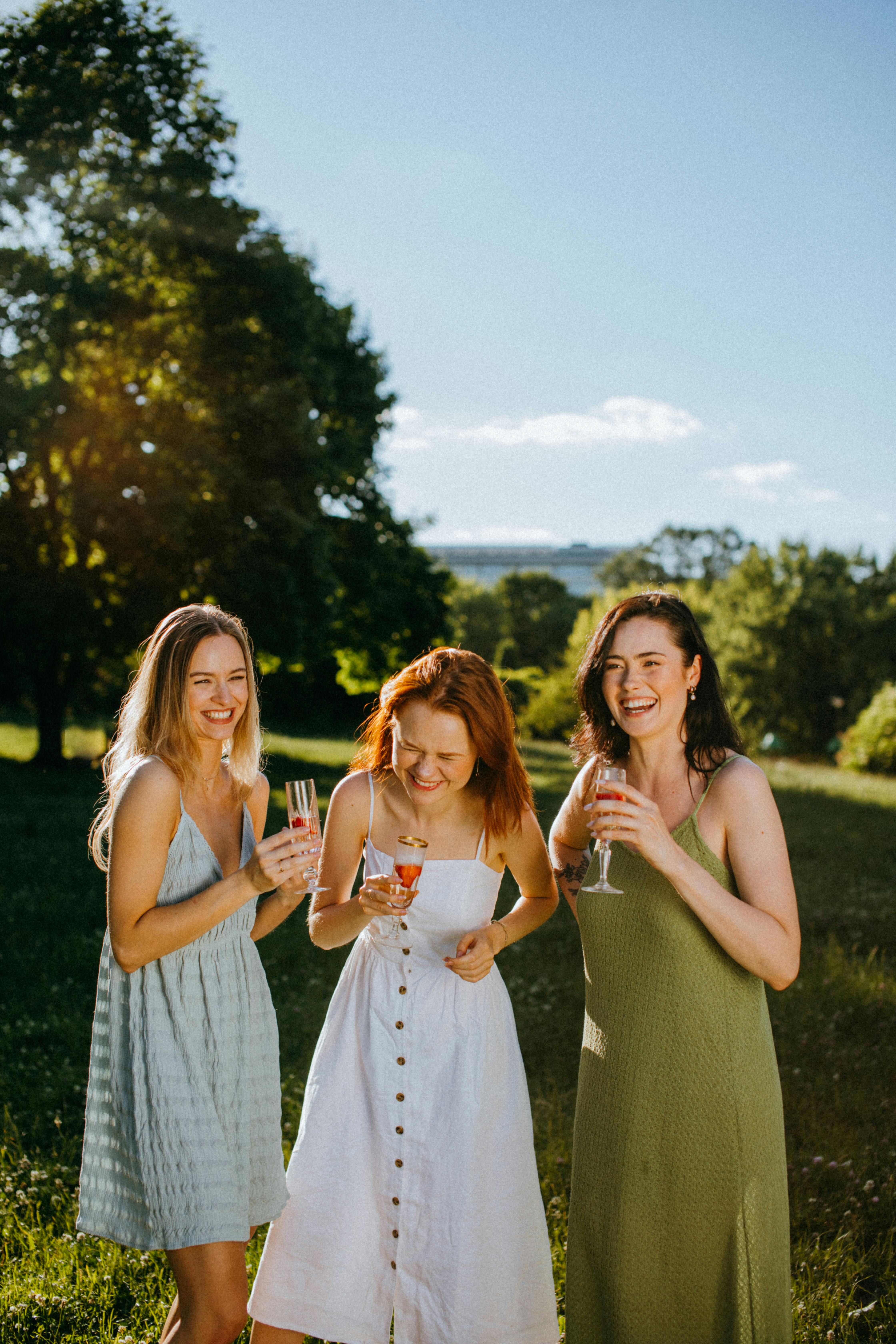 women in spaghetti strap dresses holding champagne glasses laughing