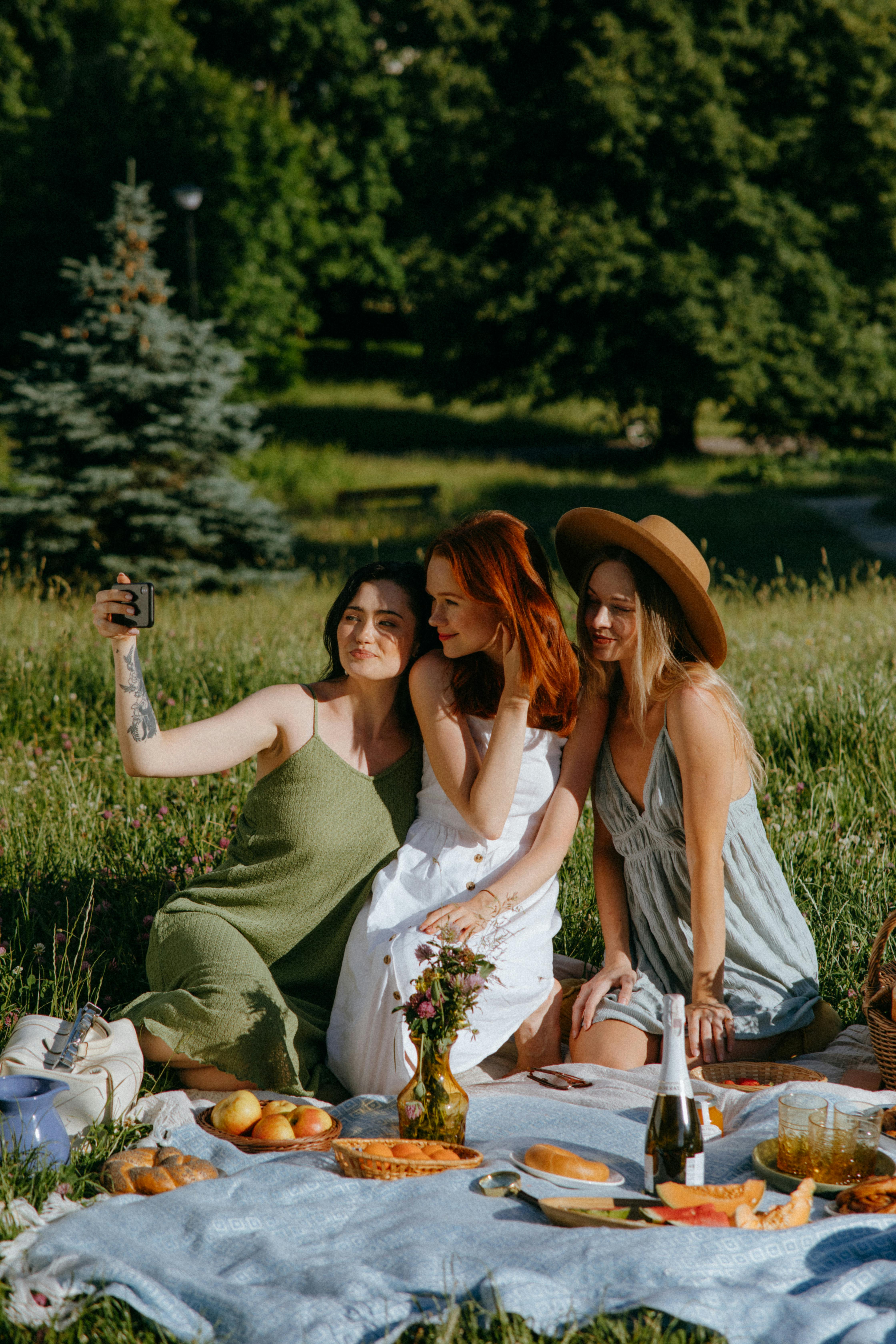 women sitting on a picnic blanket while taking a group selfie