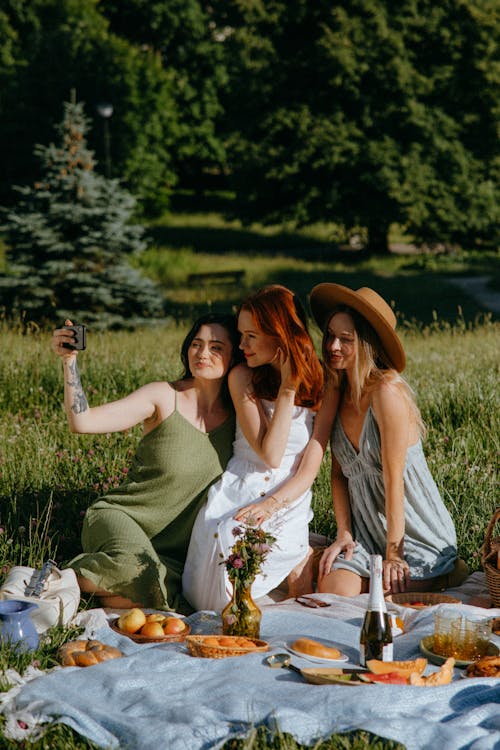 Women Sitting on a Picnic Blanket while Taking a Group Selfie