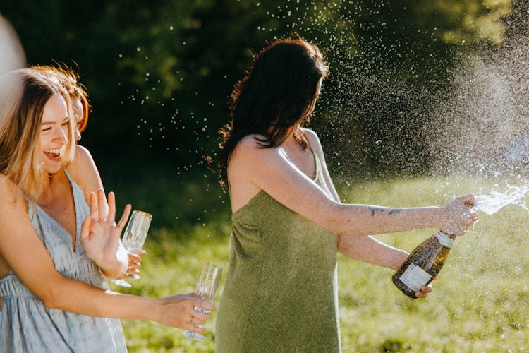 A Woman In Green Dress Popping A Champagne Bottle