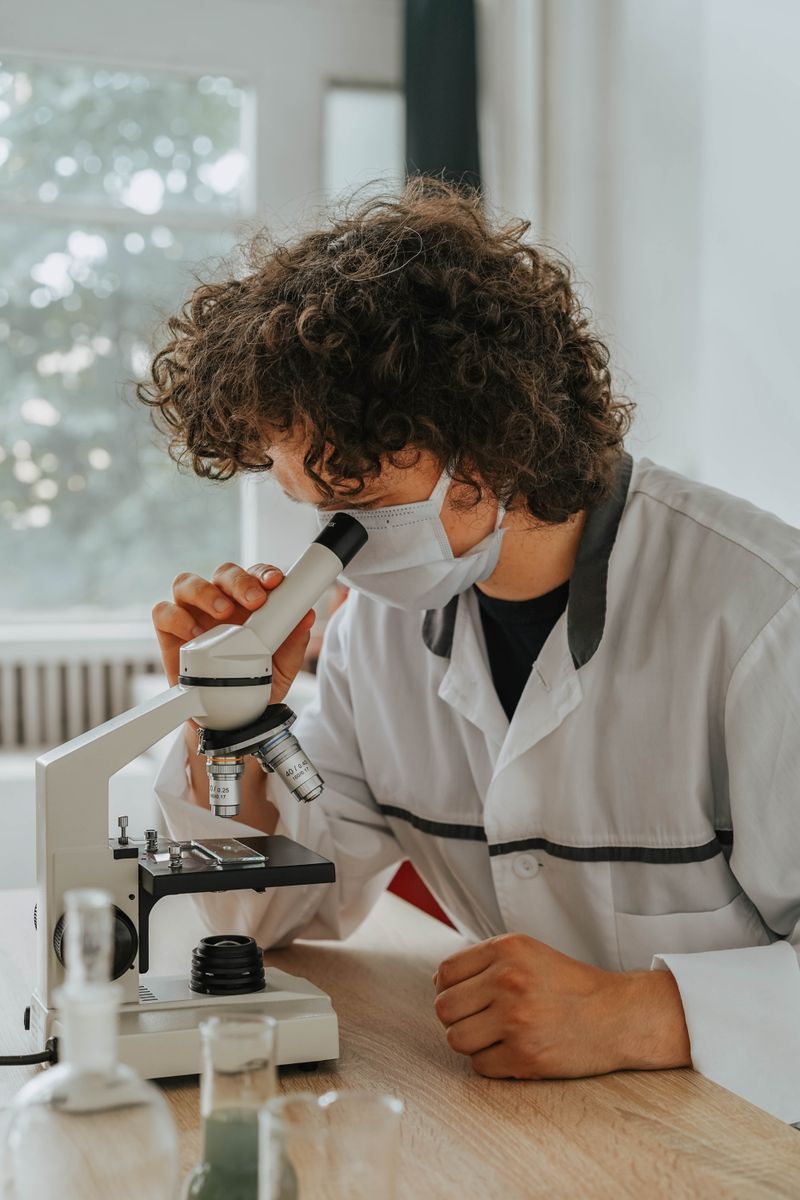 A scientist in lab coat examines samples using a microscope indoors, depicting focused research.