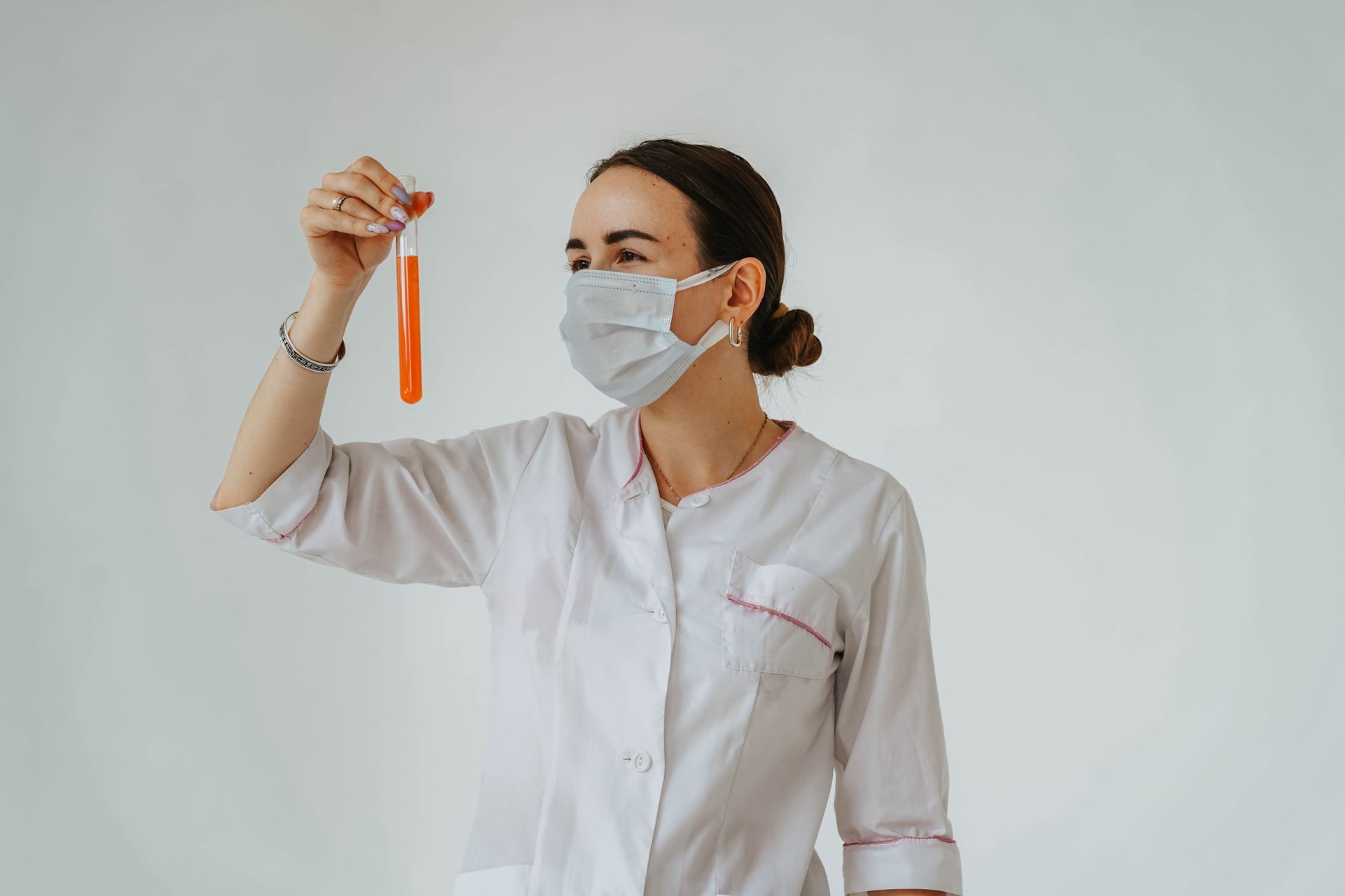 Woman in White Lab Gown Wearing Face Mask while Holding a Test Tube