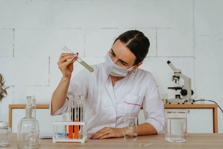 Woman In White Lab Gown Wearing Face Mask While Holding A Test Tube