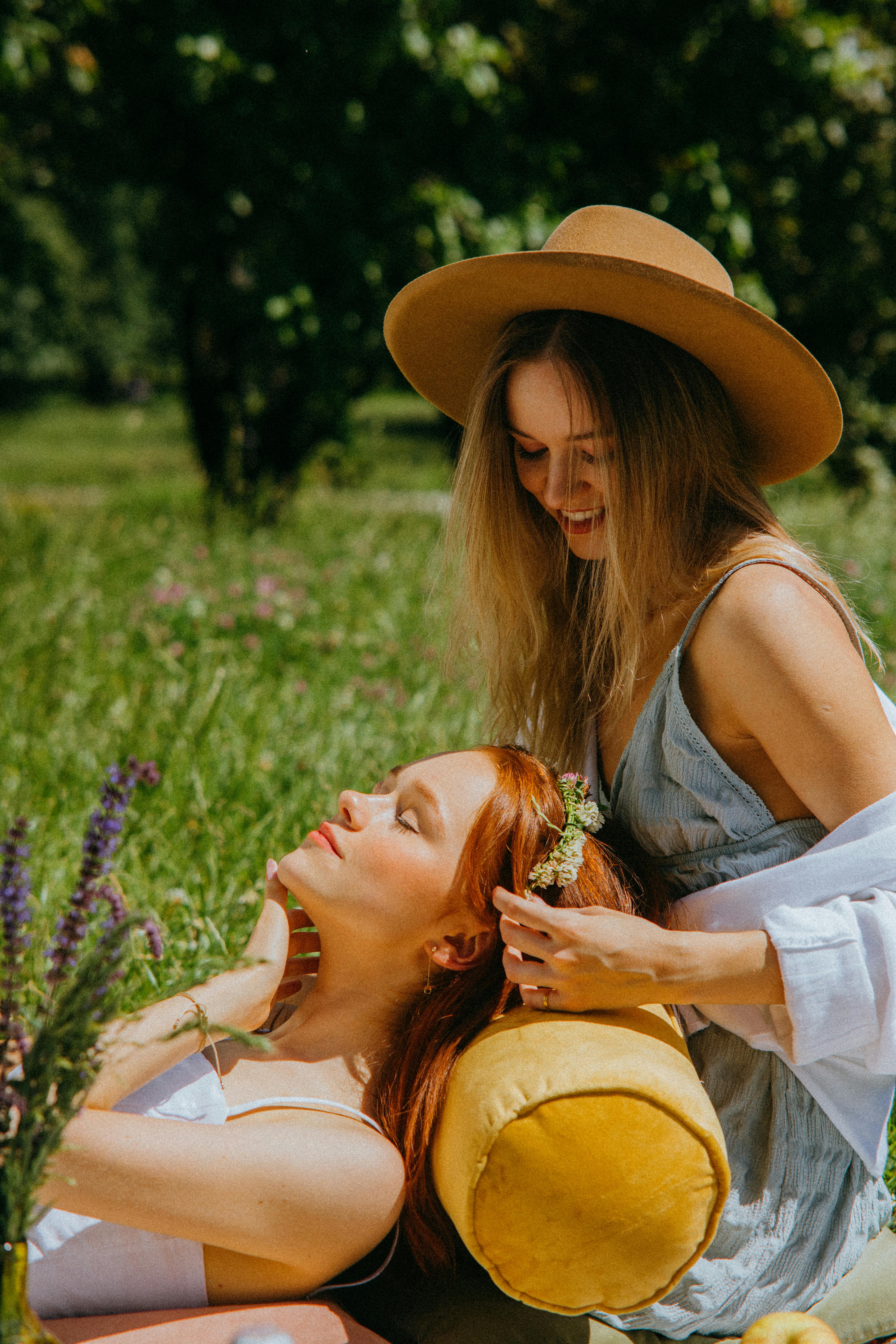 a woman in brown hat looking at the woman lying on her lap