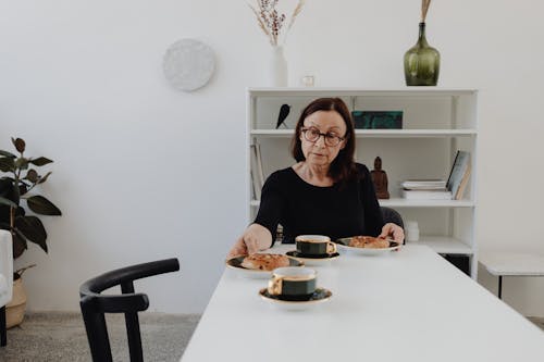 A Sad Woman in Black Long Sleeves Sitting while Looking at the Food on the Table