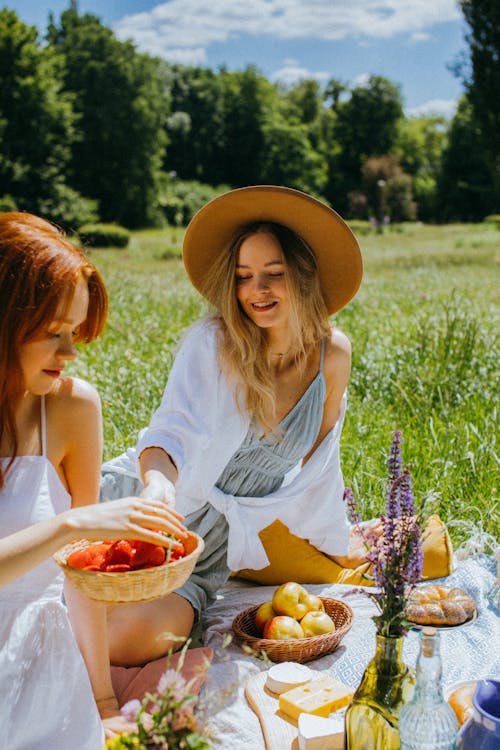 Free Women Sitting on a Picnic Blanket while Eating Stock Photo