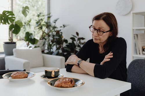 Free A Sad Woman in Black Long Sleeves Sitting while Looking at the Food on the Table Stock Photo