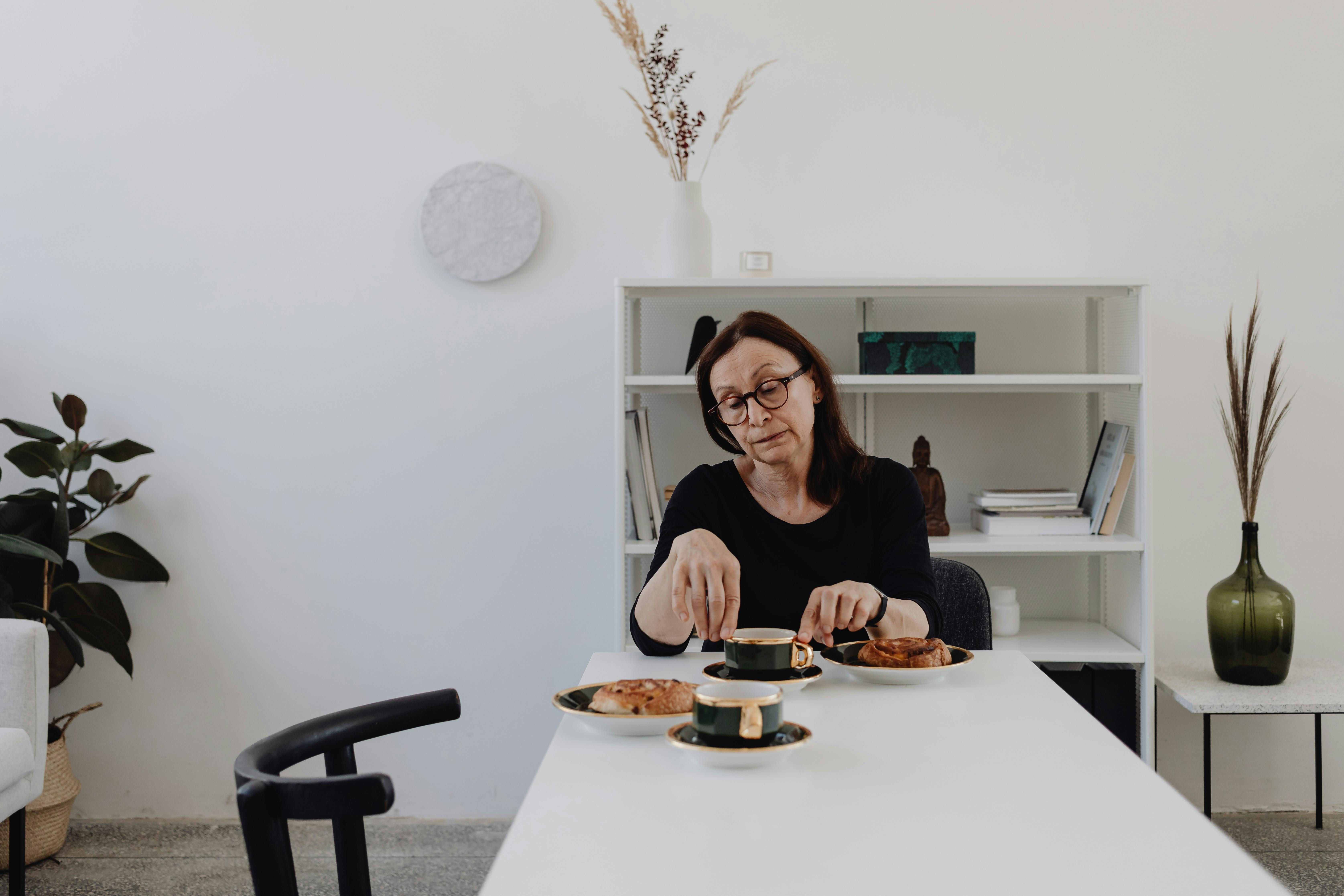 Woman reflecting deeply while having tea in a modern, minimalist dining setup.