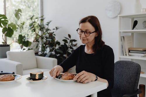 A Woman in Black Long Sleeves Sitting while Looking at the Food on the Table
