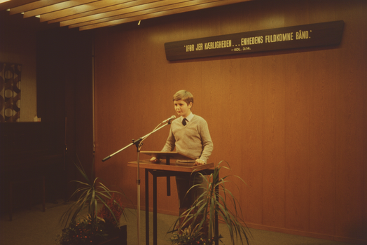 A young boy stands confidently at a podium delivering a speech indoors.