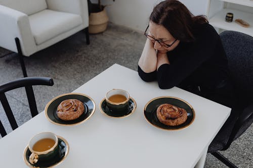 A Sad Woman in Black Long Sleeves Sitting while Looking at the Food on the Table