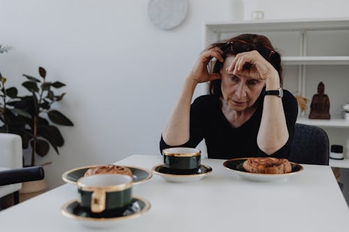 A Sad Woman in Black Long Sleeves Sitting while Looking at the Food on the Table