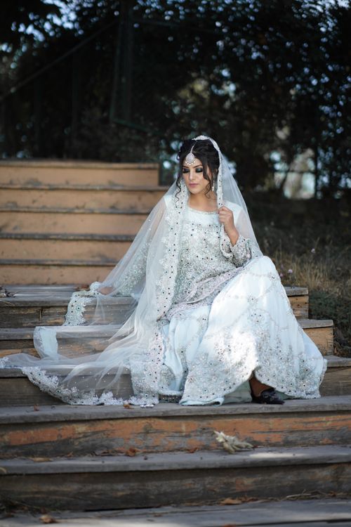 Free A bride in an ornate bridal gown sits on wooden stairs, surrounded by natural beauty in Srinagar. Stock Photo