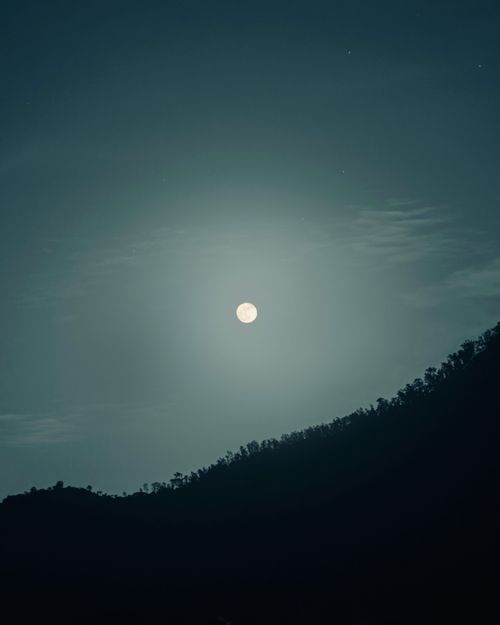 Free A tranquil night scene featuring a full moon illuminating the silhouette of a mountainscape. Stock Photo