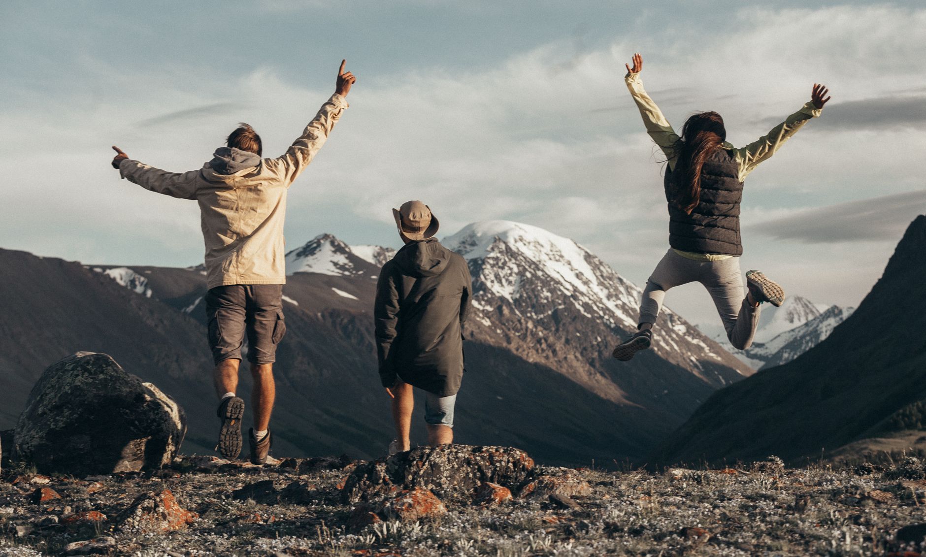 Three people enjoying a hike in snow-capped mountains, jumping with joy filled with adventure.