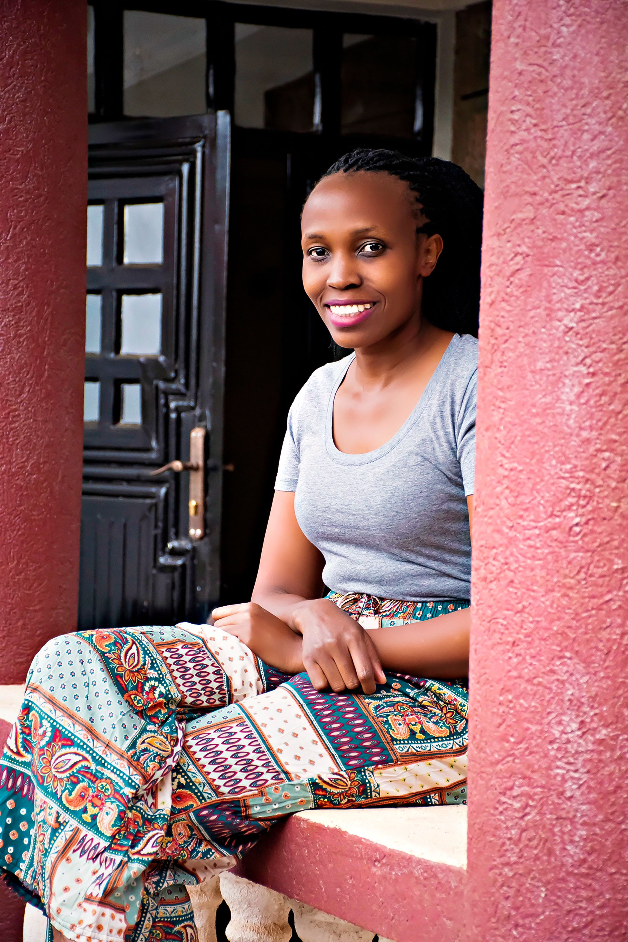 A joyful woman in a vibrant skirt sits on a porch, exuding warmth and happiness.