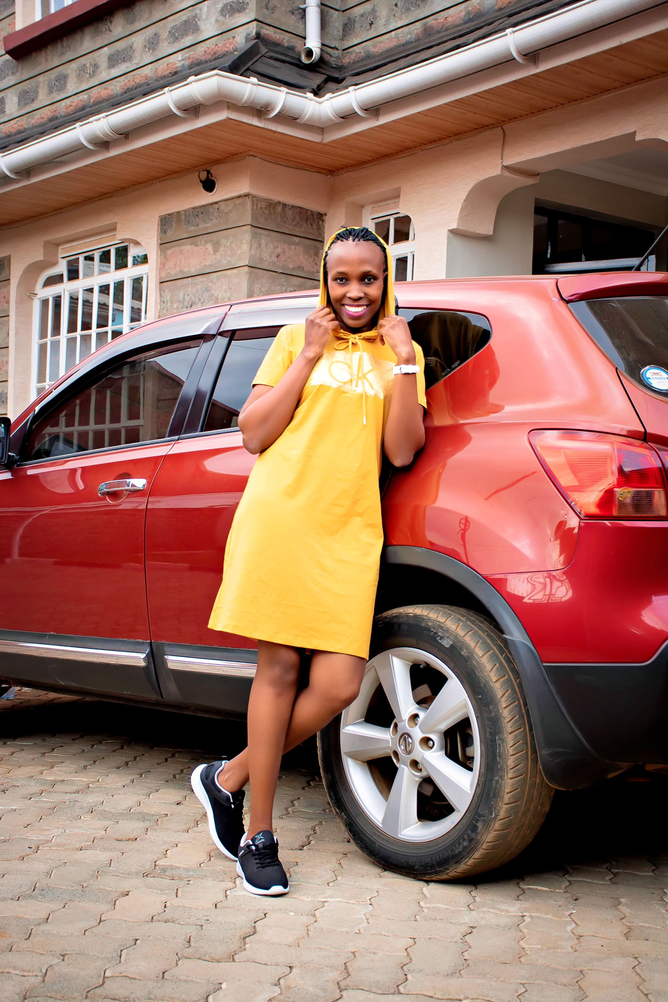 A cheerful woman in a yellow dress posing beside a red SUV outdoors.