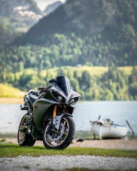 A sleek sports motorcycle parked by a serene lake with mountains in the background.