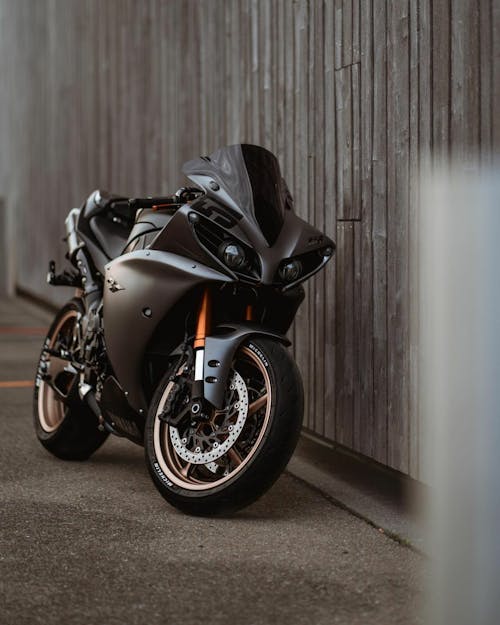Black and Orange Sports Bike Parked Beside Brown Wooden Wall