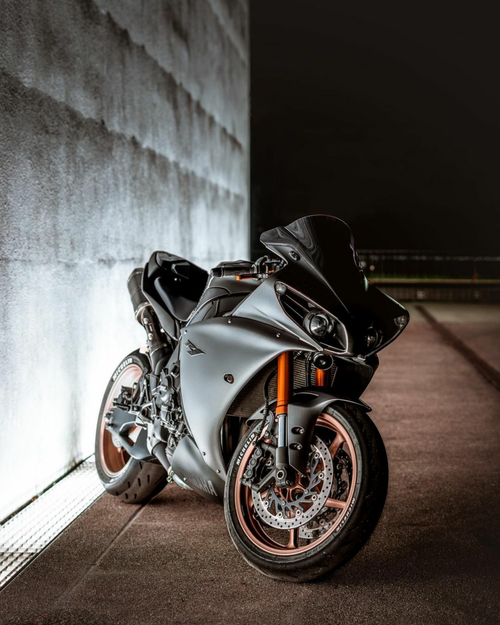 Free A modern sports motorcycle with chrome accents parked against a wall at night, showcasing its sleek design. Stock Photo