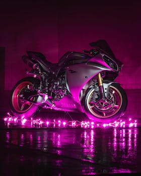 A stylish motorcycle illuminated by neon pink lights in a dramatic dark setting.