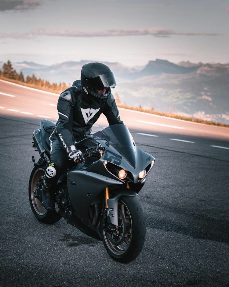 A Person In Black Helmet Riding A Black Sports Bike On The Road