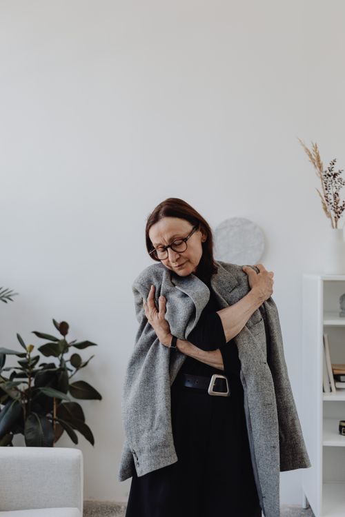 Free Senior woman indoors embracing gray coat, expressing introspective emotion. Stock Photo