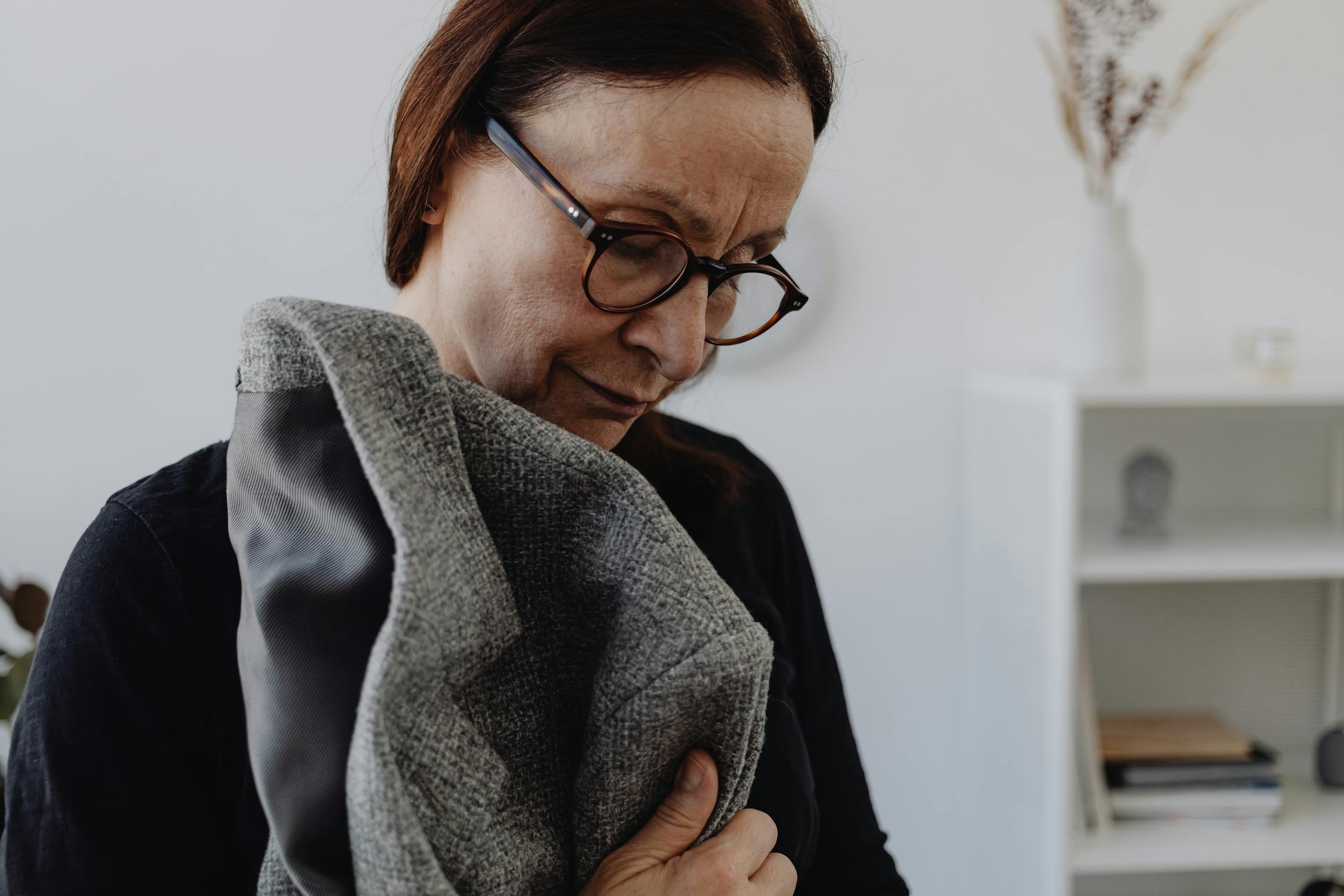An Elderly Woman in Black Shirt Wearing Eyeglasses while Holding a Coat