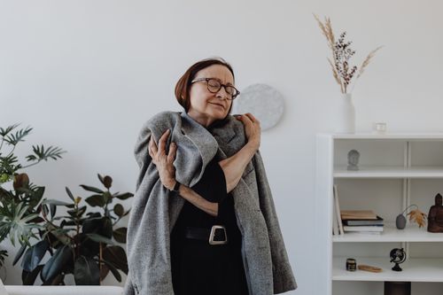 Free Smiling elderly woman in a black dress embracing a grey coat, conveying warmth. Stock Photo
