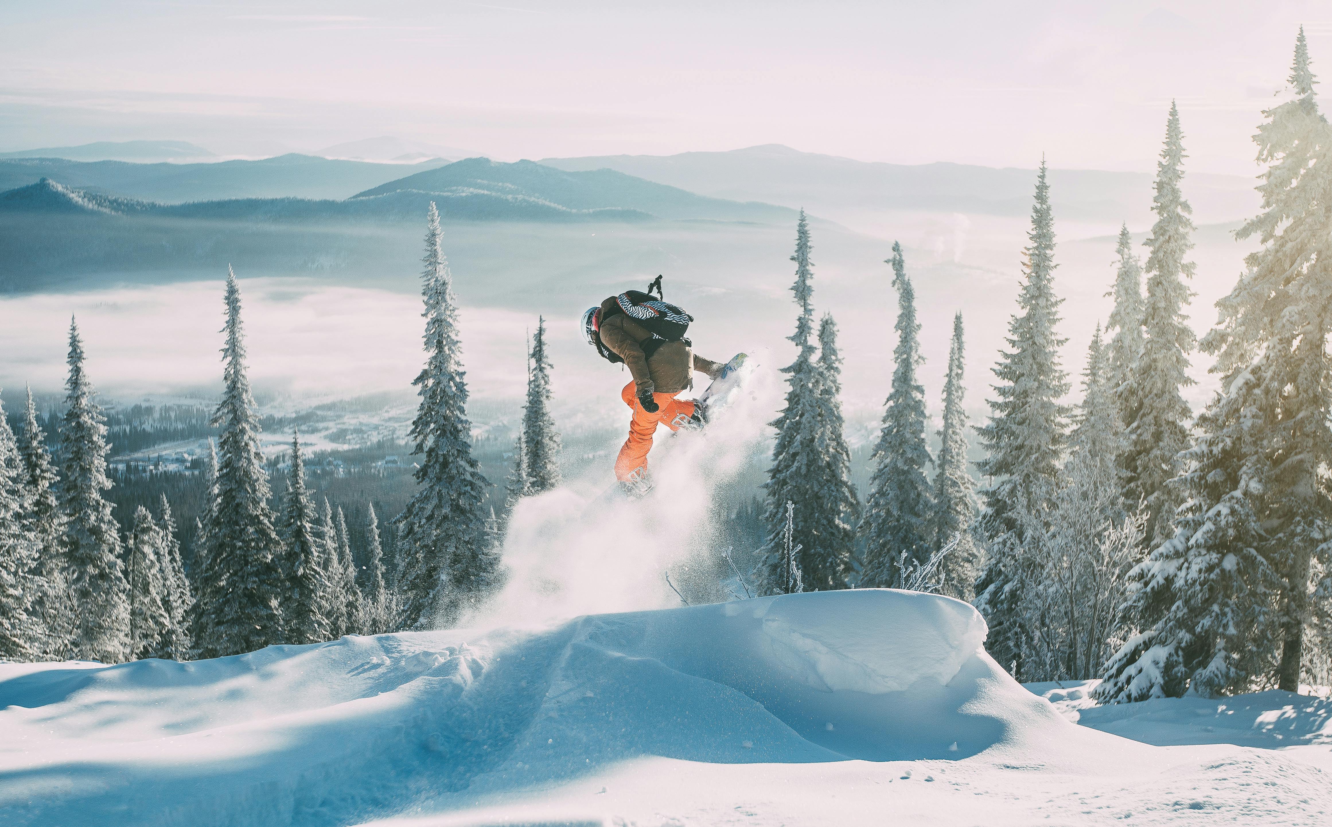 Prescription Goggle Inserts - Dynamic shot of a snowboarder mid-air amidst snowy trees and mountains in winter.