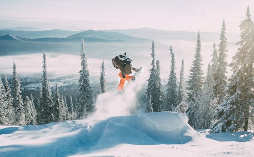 Person in Orange Jacket and Black Pants Riding on Snowboard 