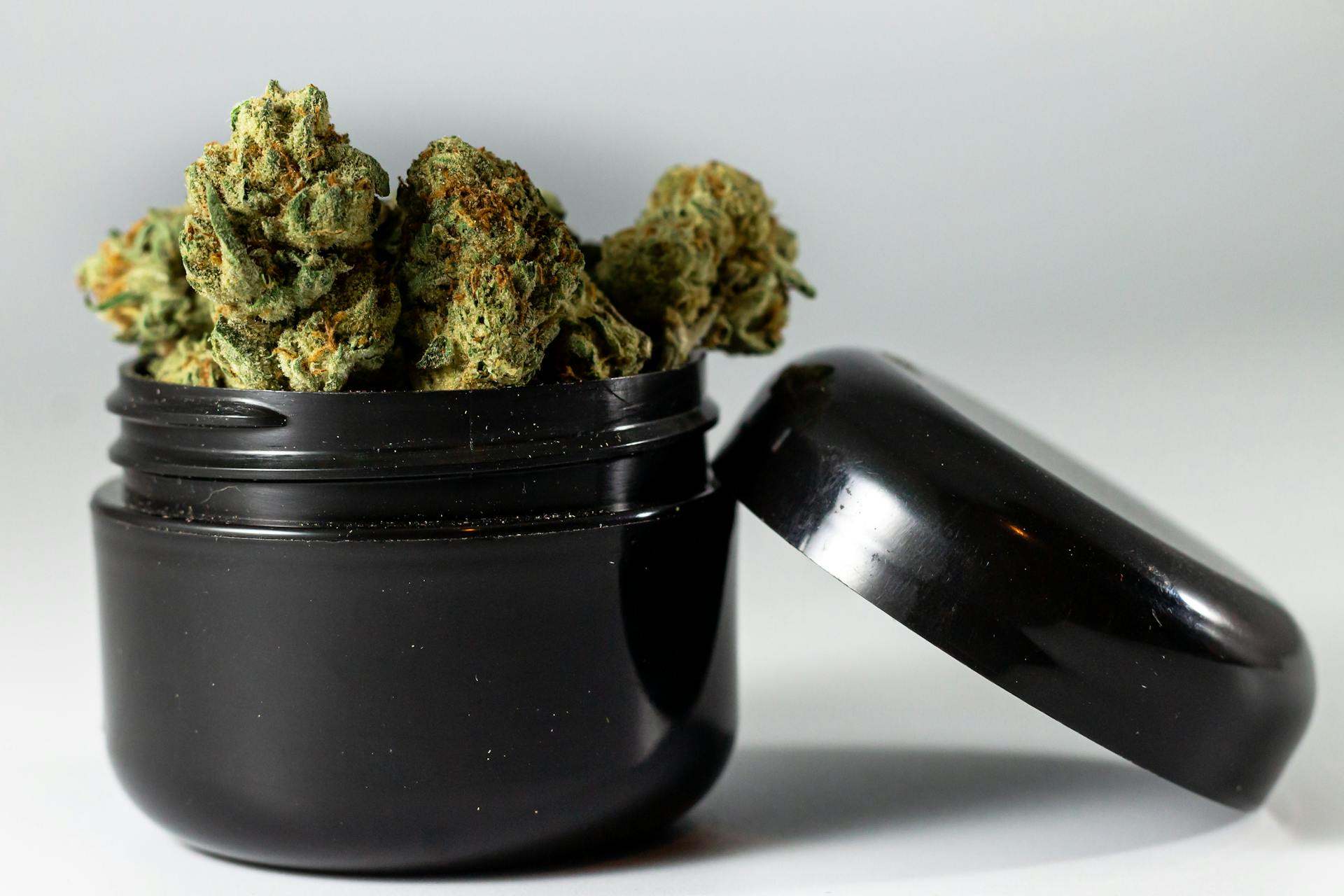 Detailed image of cannabis buds overflowing from a black jar, showcasing texture and color.