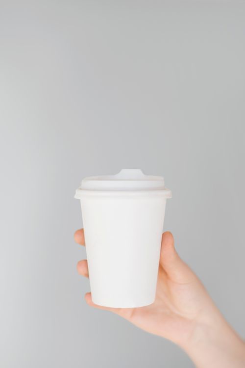 Free A minimalist image featuring a disposable coffee cup held by a hand against a plain background. Stock Photo
