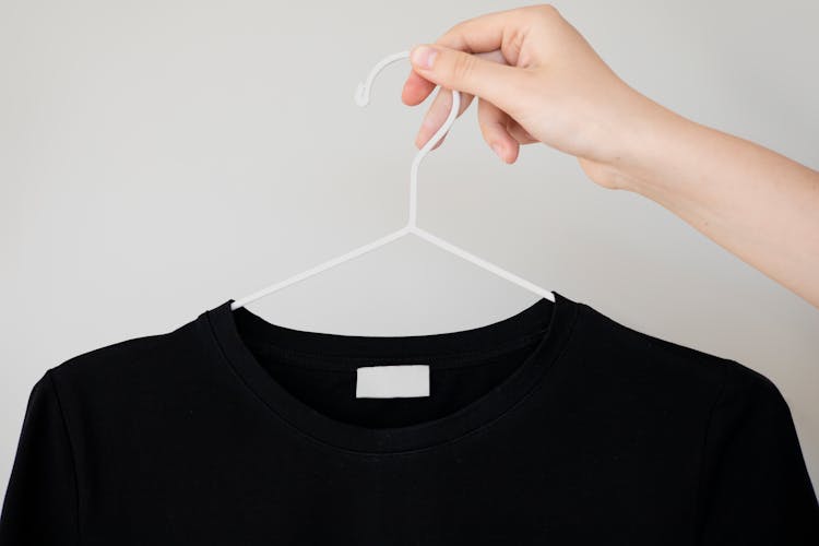 A Person Holding A Clothes Hanger With A Blank Shirt Label