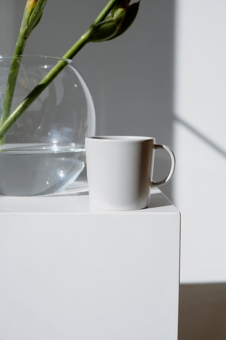 White Mug Beside A Clear Glass Vase 