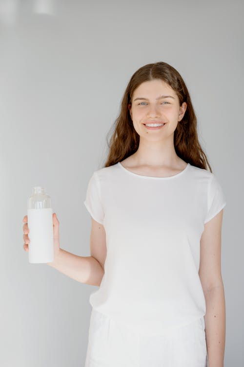 A Woman in White Shirt Smiling while Holding a Glass Bottle