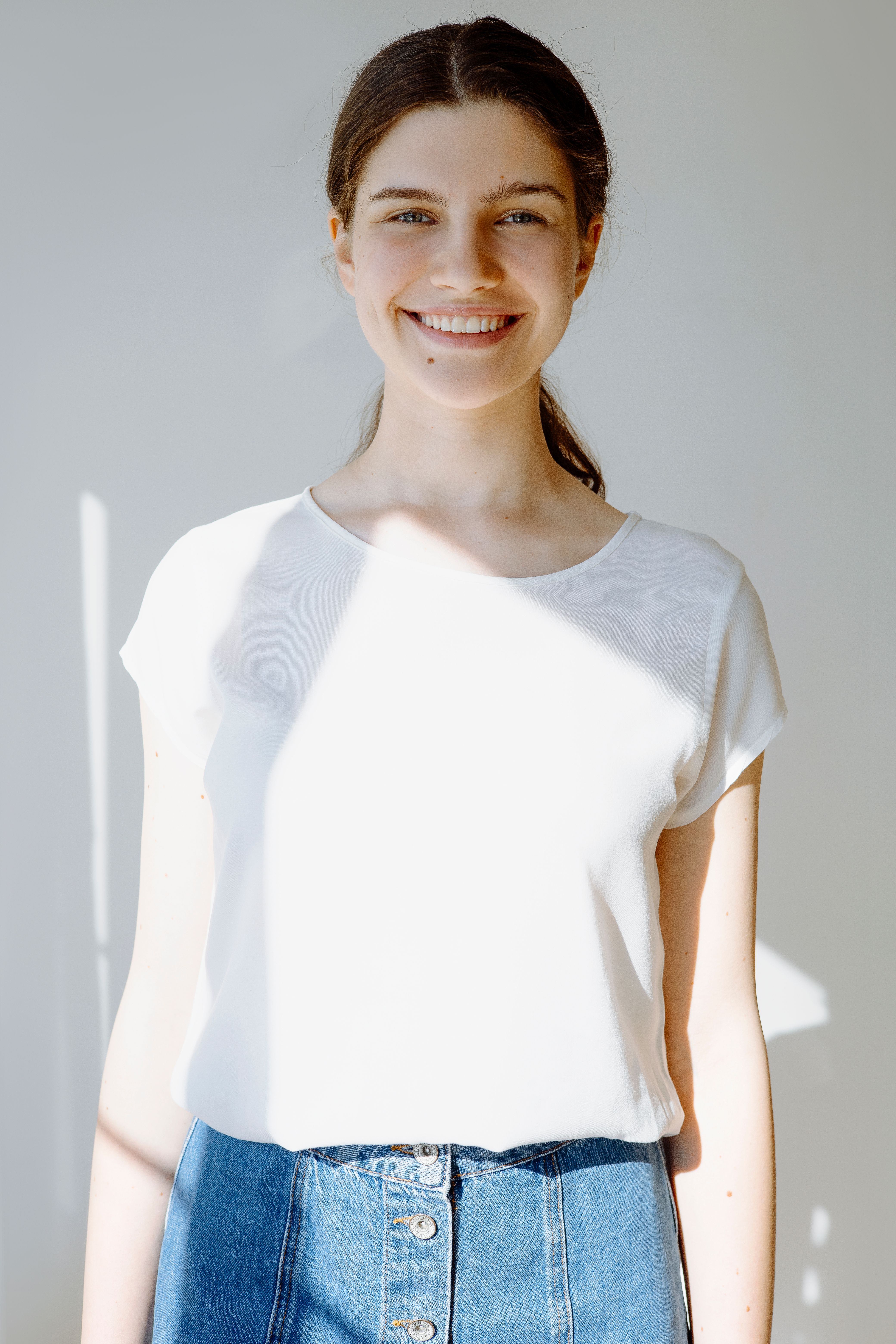 A woman in a white shirt smiles warmly in natural indoor lighting.